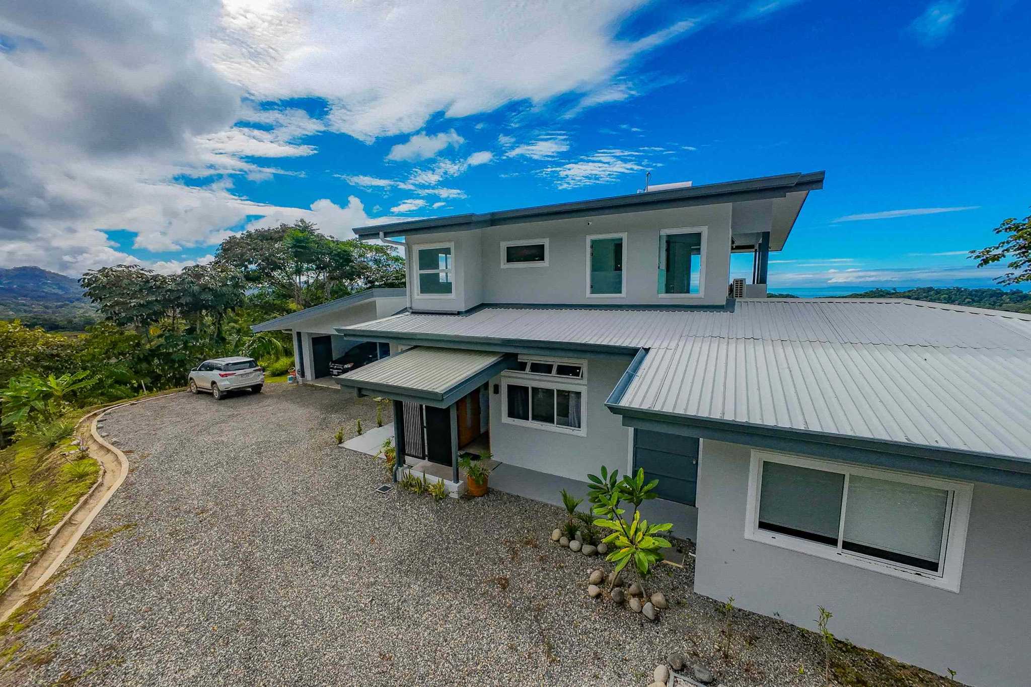 Luxury Mountain Retreat aerial view of modern two-story home with metal roof and gravel driveway in Ojochal, Costa Rica