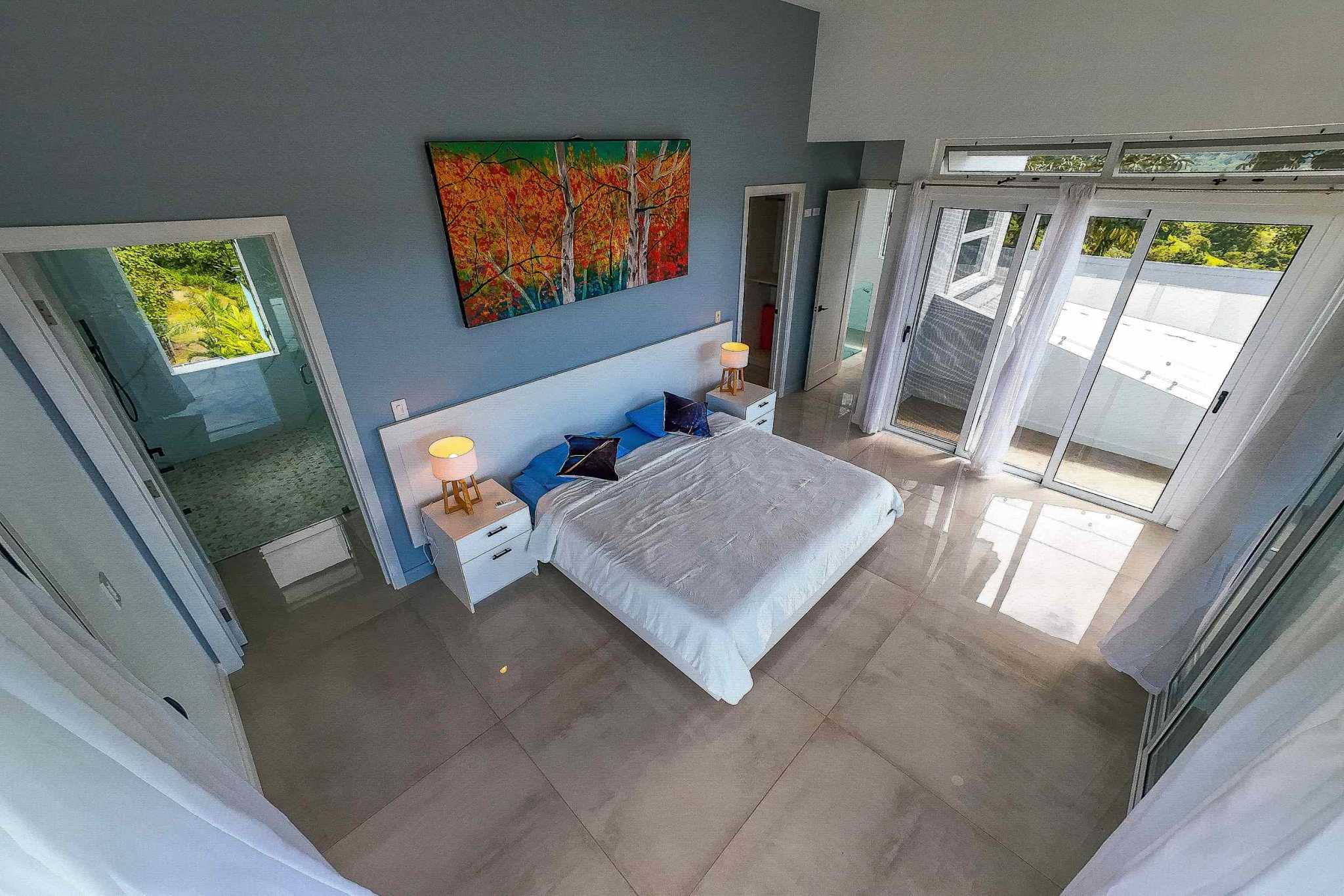 Luxury Retreat primary bedroom with king bed, glass balcony doors, and forest artwork in Ojochal, Costa Rica