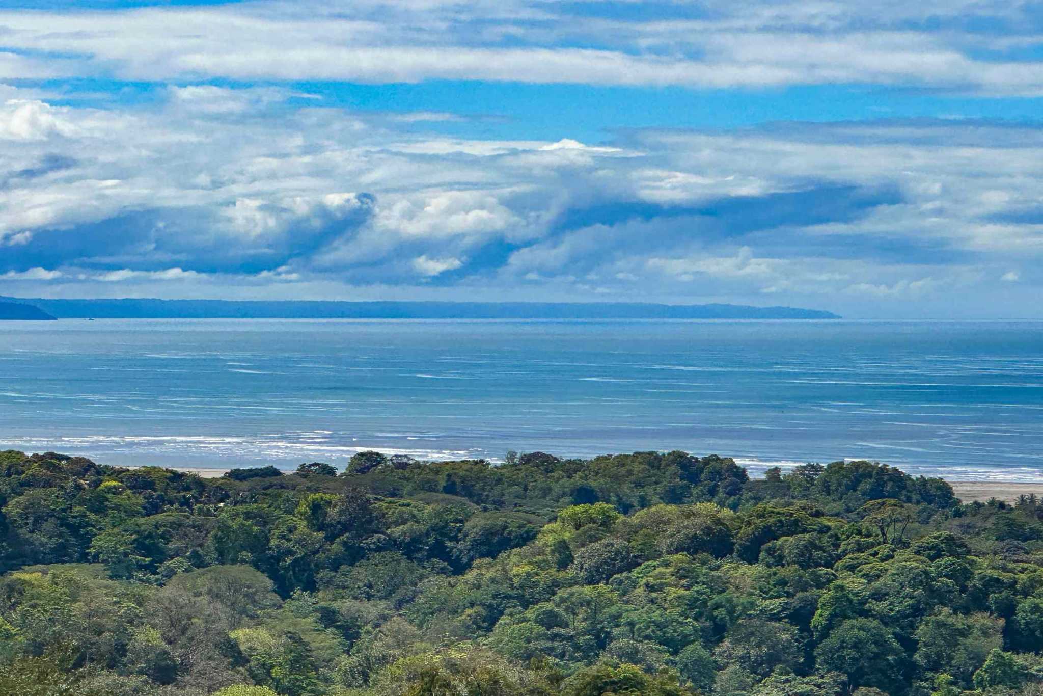 Luxury Retreat forest canopy with ocean, beach, and coastline view under cloudy sky in Ojochal, Costa Rica