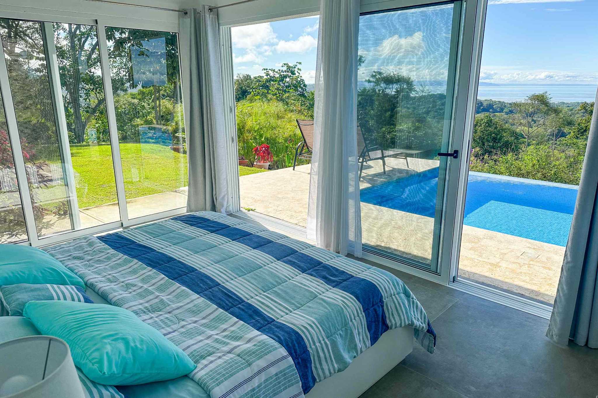 Mountain & Ocean View Retreat bedroom with glass doors overlooking pool and hills in Ojochal, Costa Rica