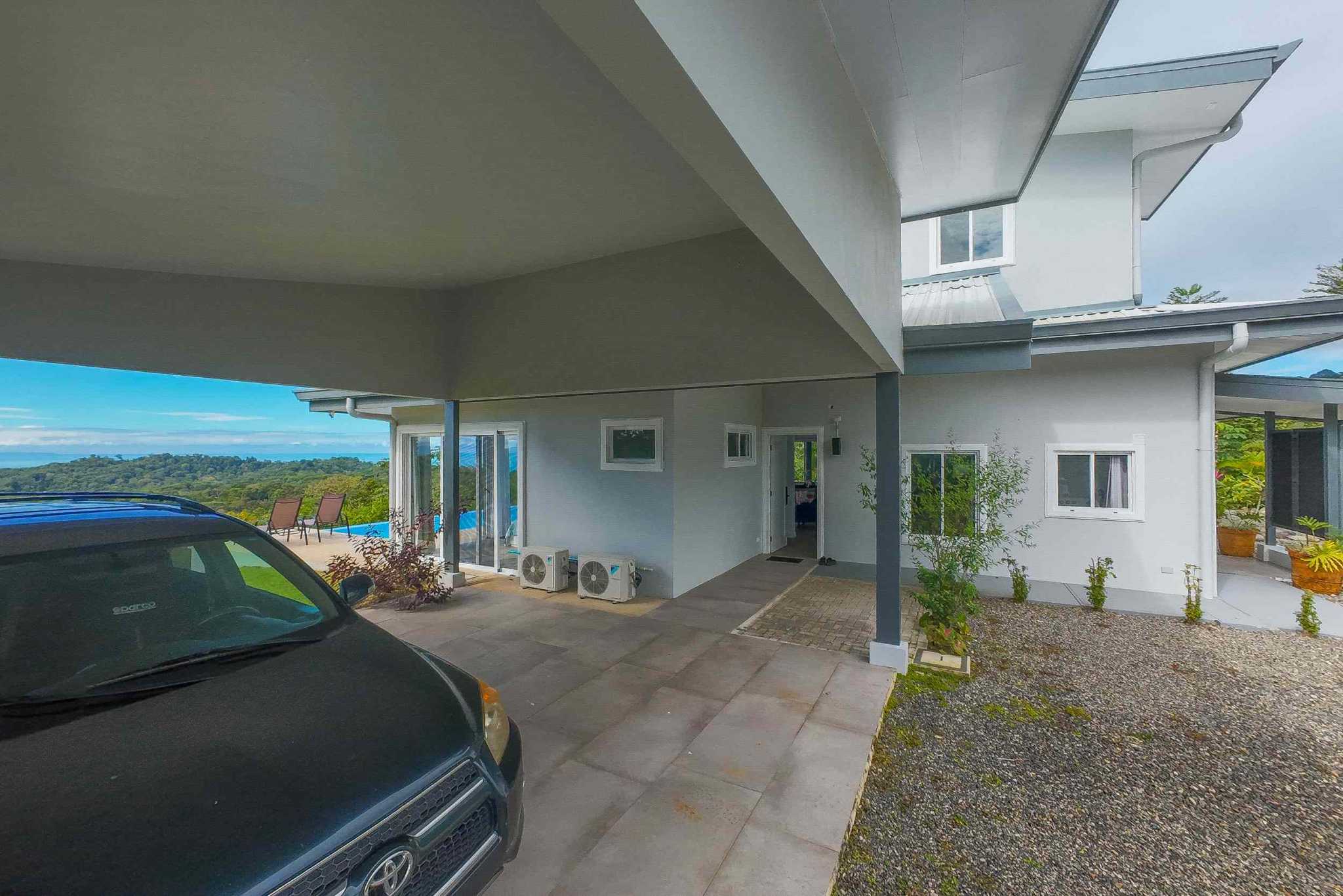 Mountain & Ocean View Home carport with parked truck, exterior walls, and distant ocean view in Ojochal, Costa Rica