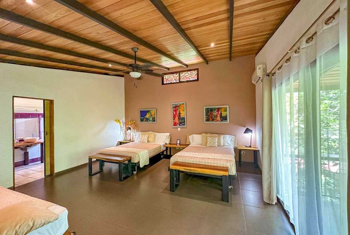 6-Bedroom Business Property bedroom with three beds, wood beam ceiling and garden glass doors in Ojochal, Costa Rica