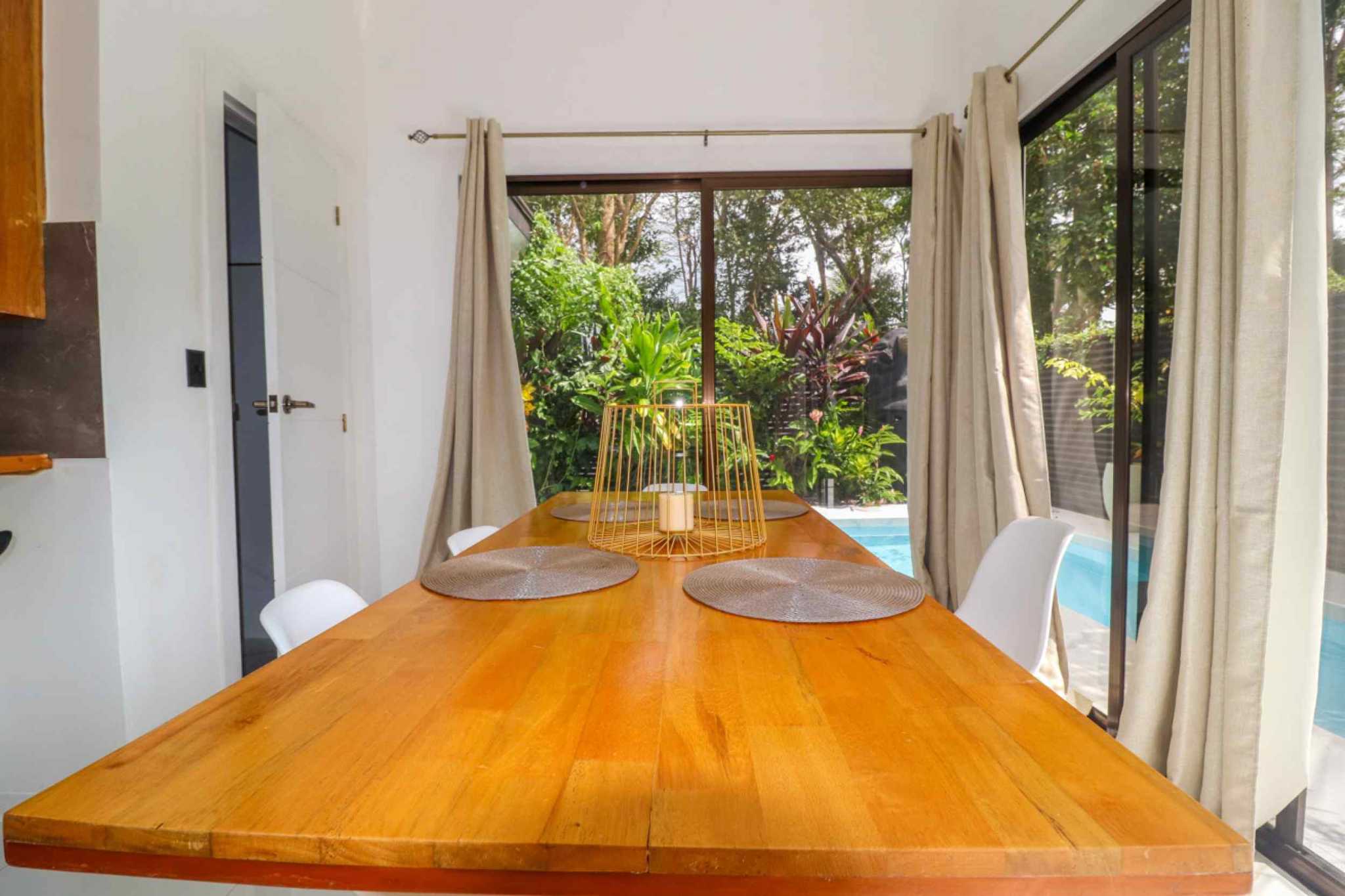 55856-10 Stunning 3-Bedroom Home dining table with white chairs beside glass doors overlooking garden and pool in Bahia, Costa Rica