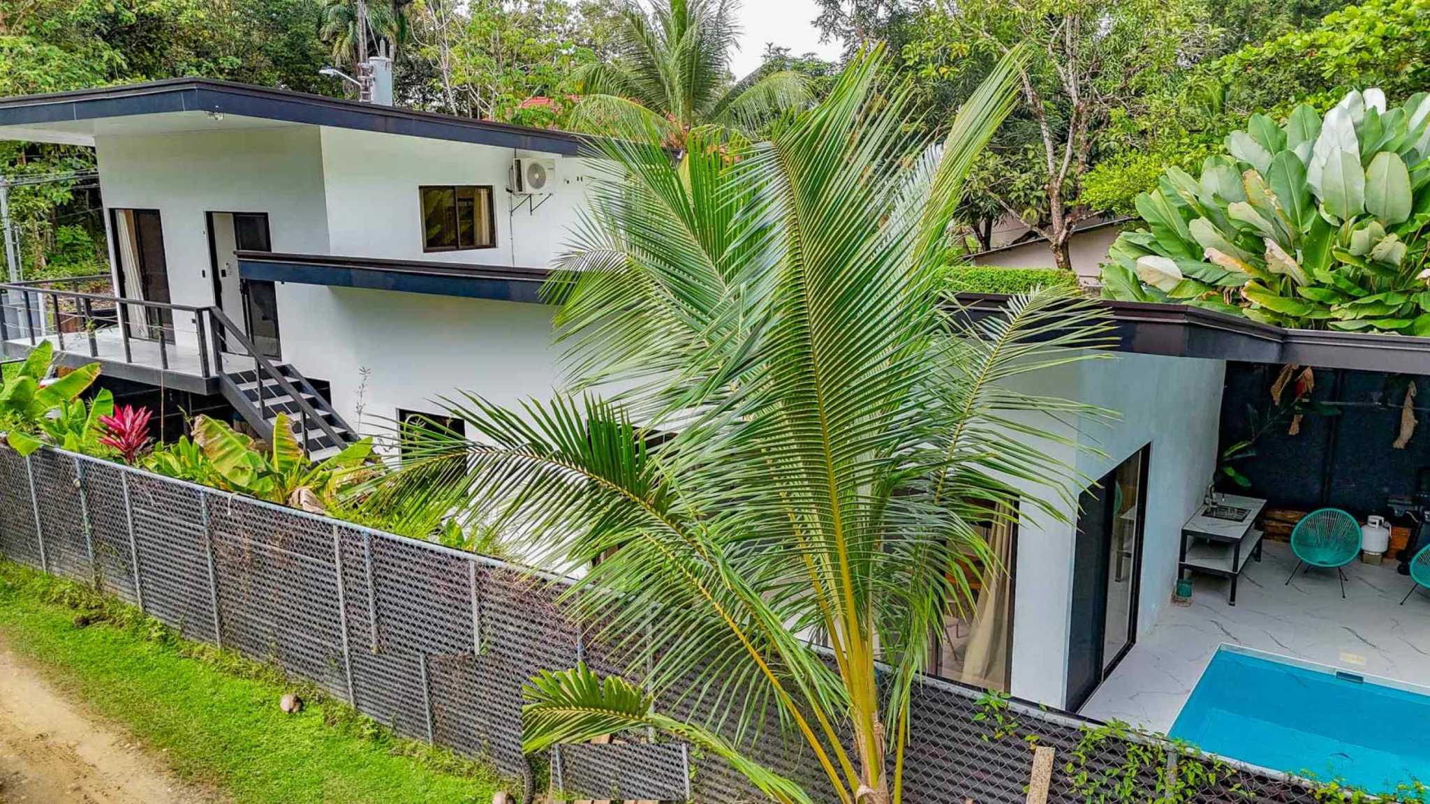 55856-1 3-Bedroom Home with Pool: white two-story exterior, balcony, staircase, patio and turquoise pool among palms in Bahia, Costa Rica
