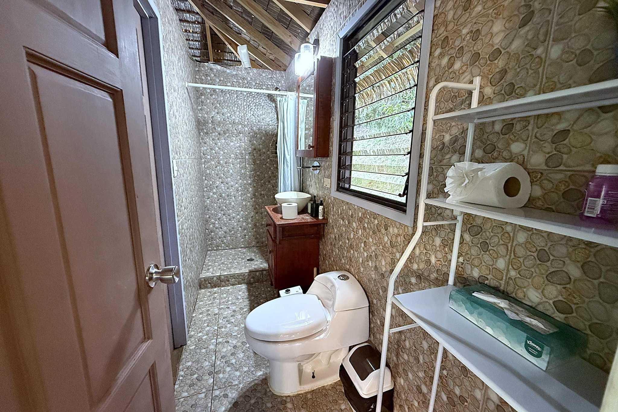 65486-24 Jungle Sanctuary bathroom with pebble tile shower, wooden vanity and jungle-view window in Ojochal, Costa Rica
