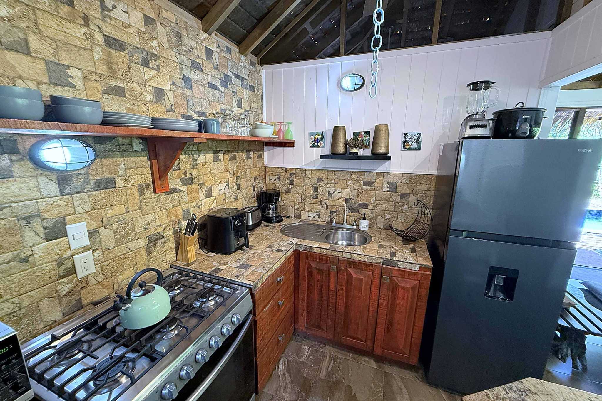 65486-16 Jungle Sanctuary kitchen with stone walls, gas range, sink, and fridge under wood beams in Ojochal, Costa Rica