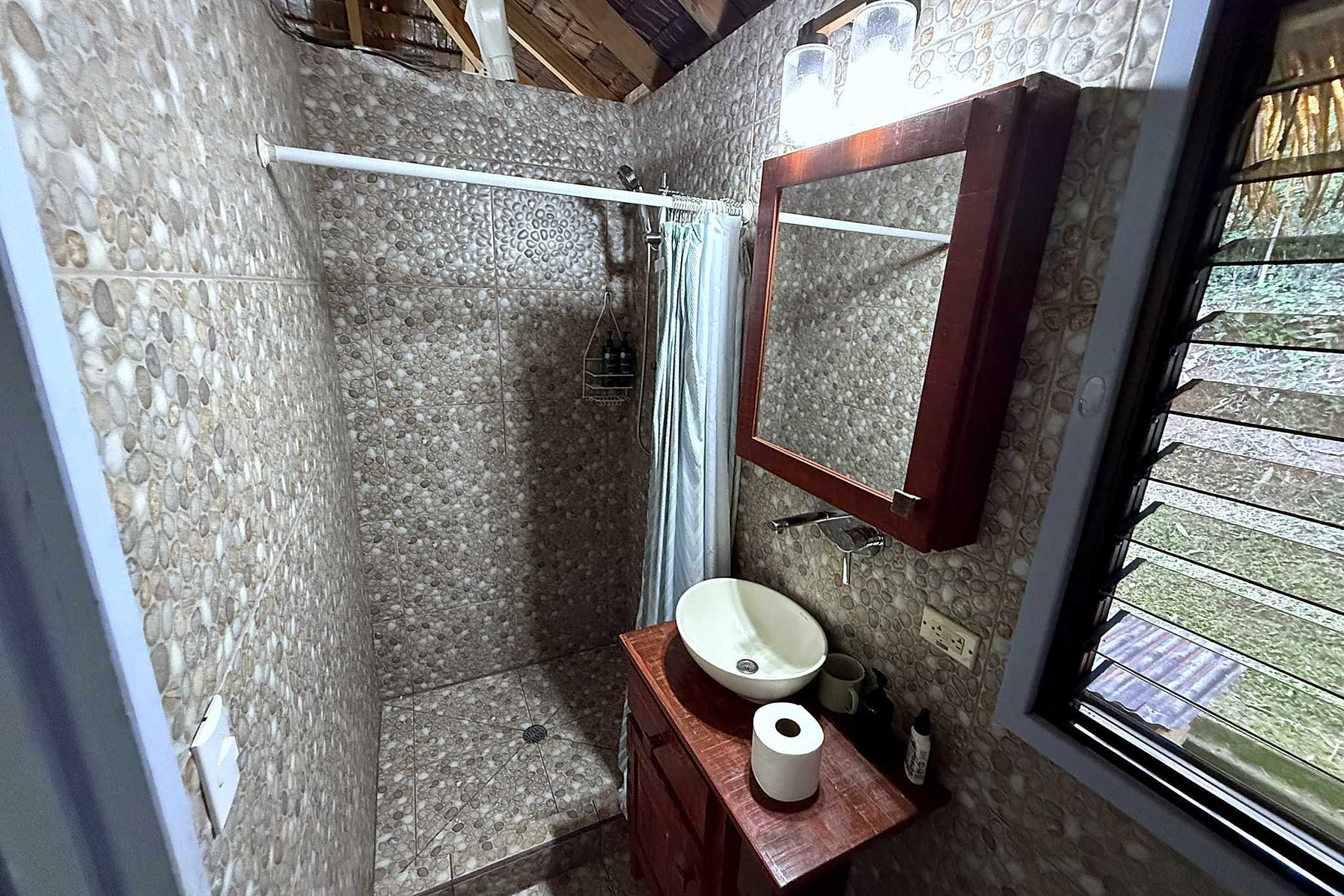 65486-22 Jungle Sanctuary Retreat pebble-tiled bathroom with walk-in shower, vessel sink and jungle-view window in Ojochal, Costa Rica