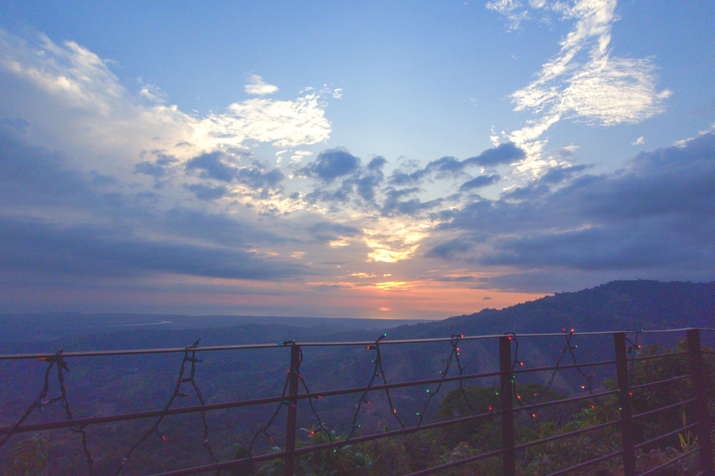 Panoramic sunset views over the ocean and mountains from a terrace railing in Toucan Valley, Costa Rica.