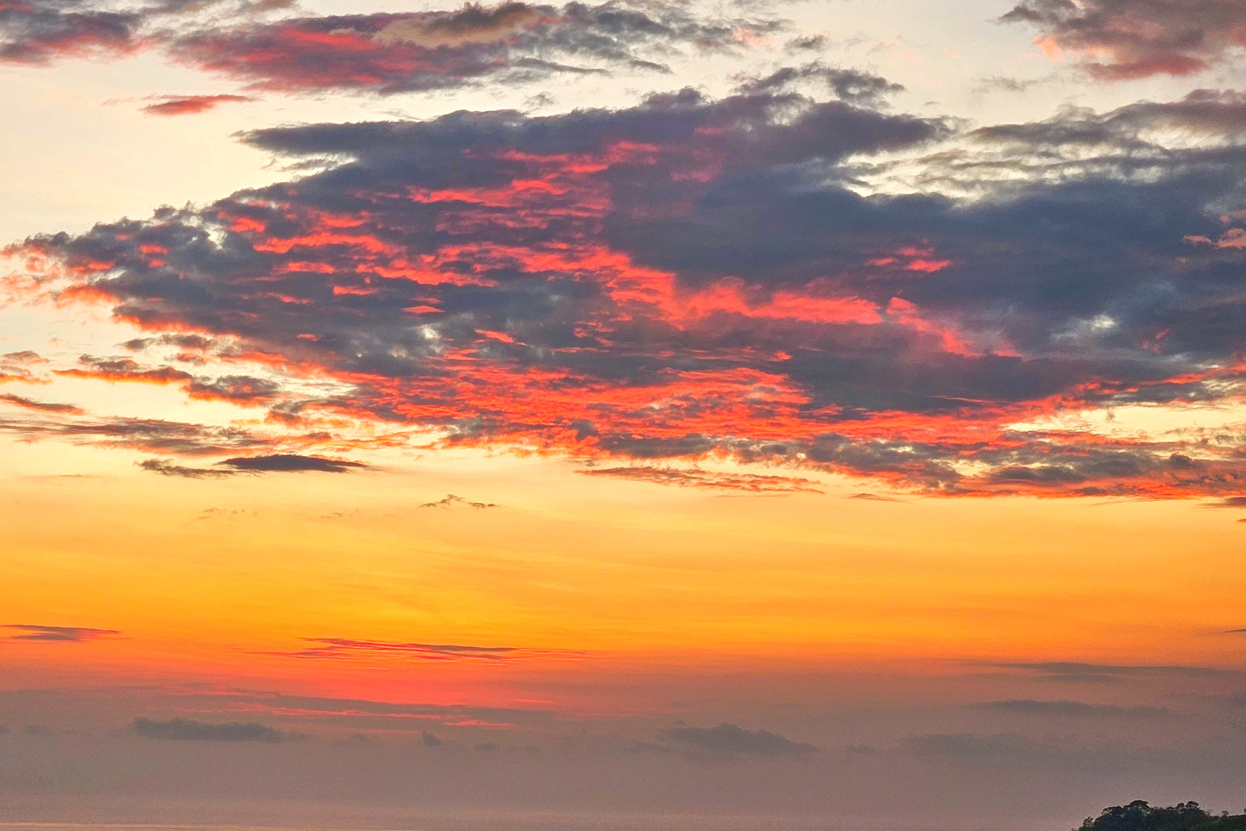 Vibrant orange sunset over the ocean and forested hills in Toucan Valley, Costa Rica.