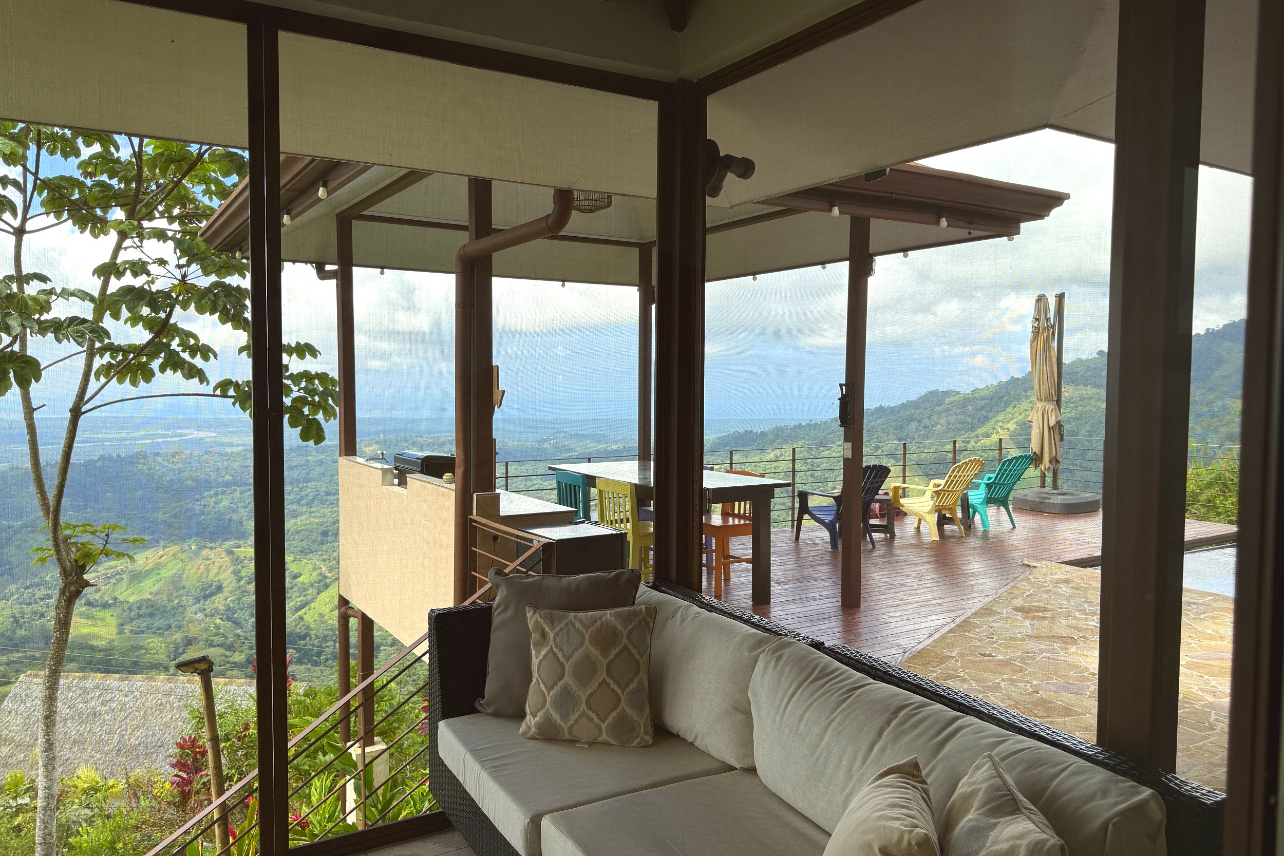 Indoor seating area facing a wooden terrace with panoramic mountain and ocean views in Toucan Valley.