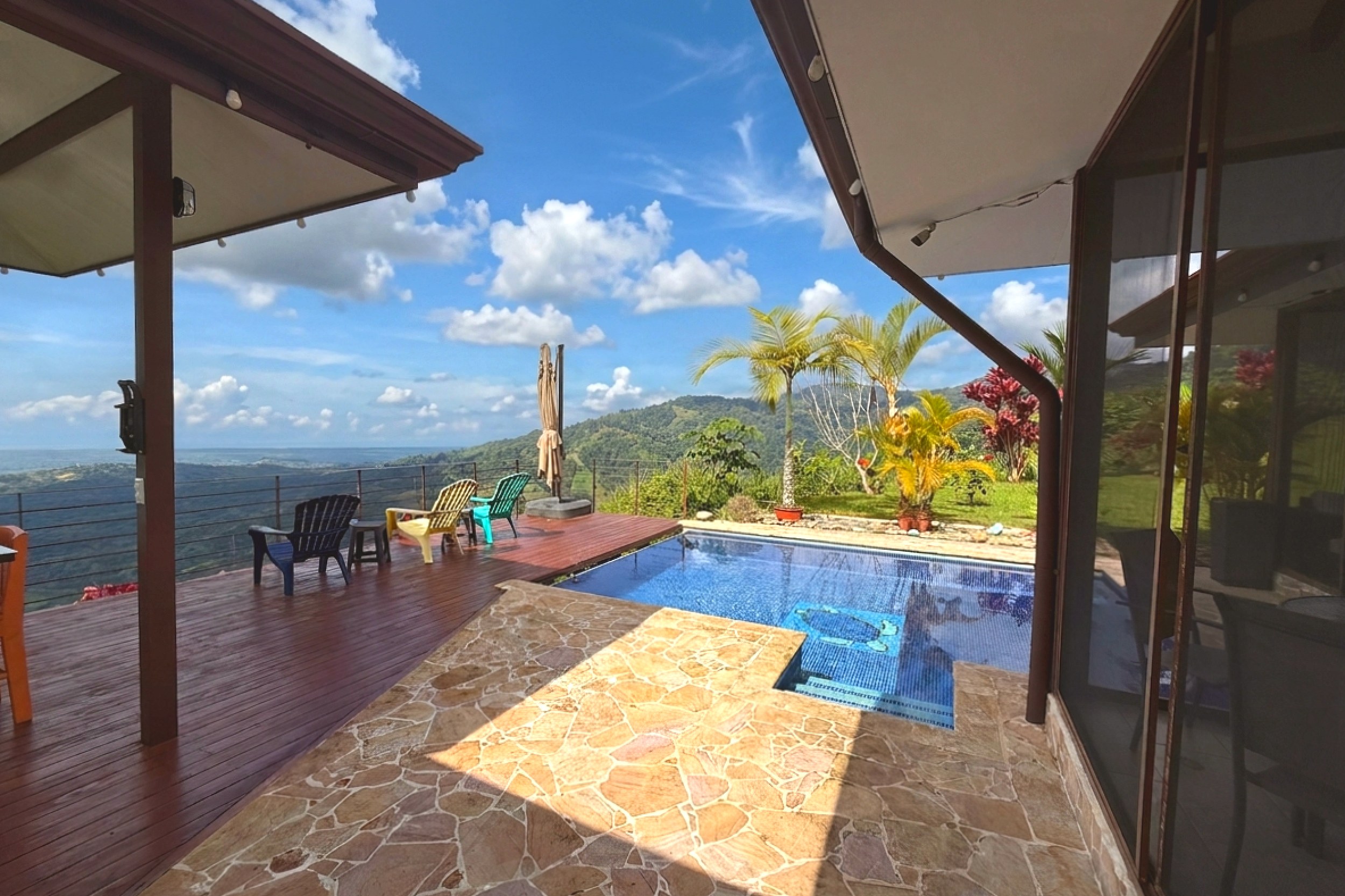 Panoramic valley and mountain views from a wooden deck with colorful chairs in Toucan Valley, Costa Rica.