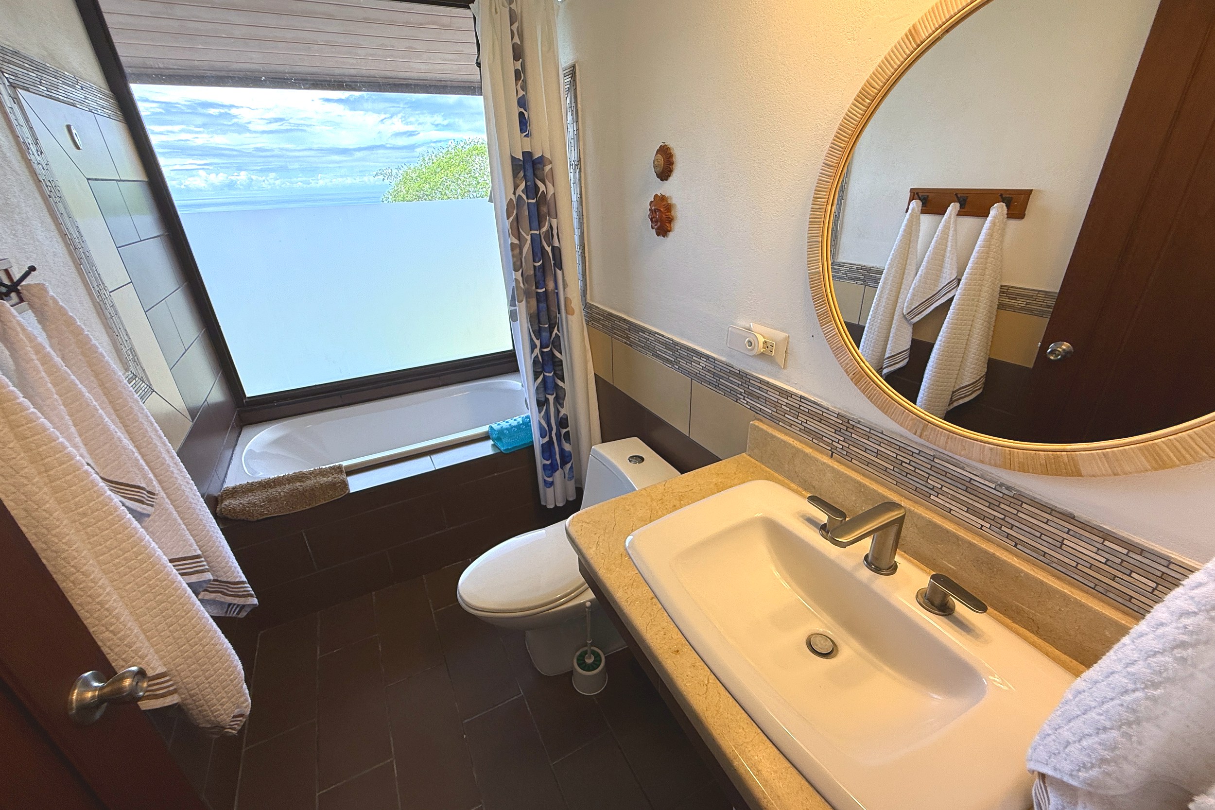 Ocean-View Guest Bathroom Ocean View Home bathroom with tub, ocean-view window & round mirror in Ojochal, Costa Rica