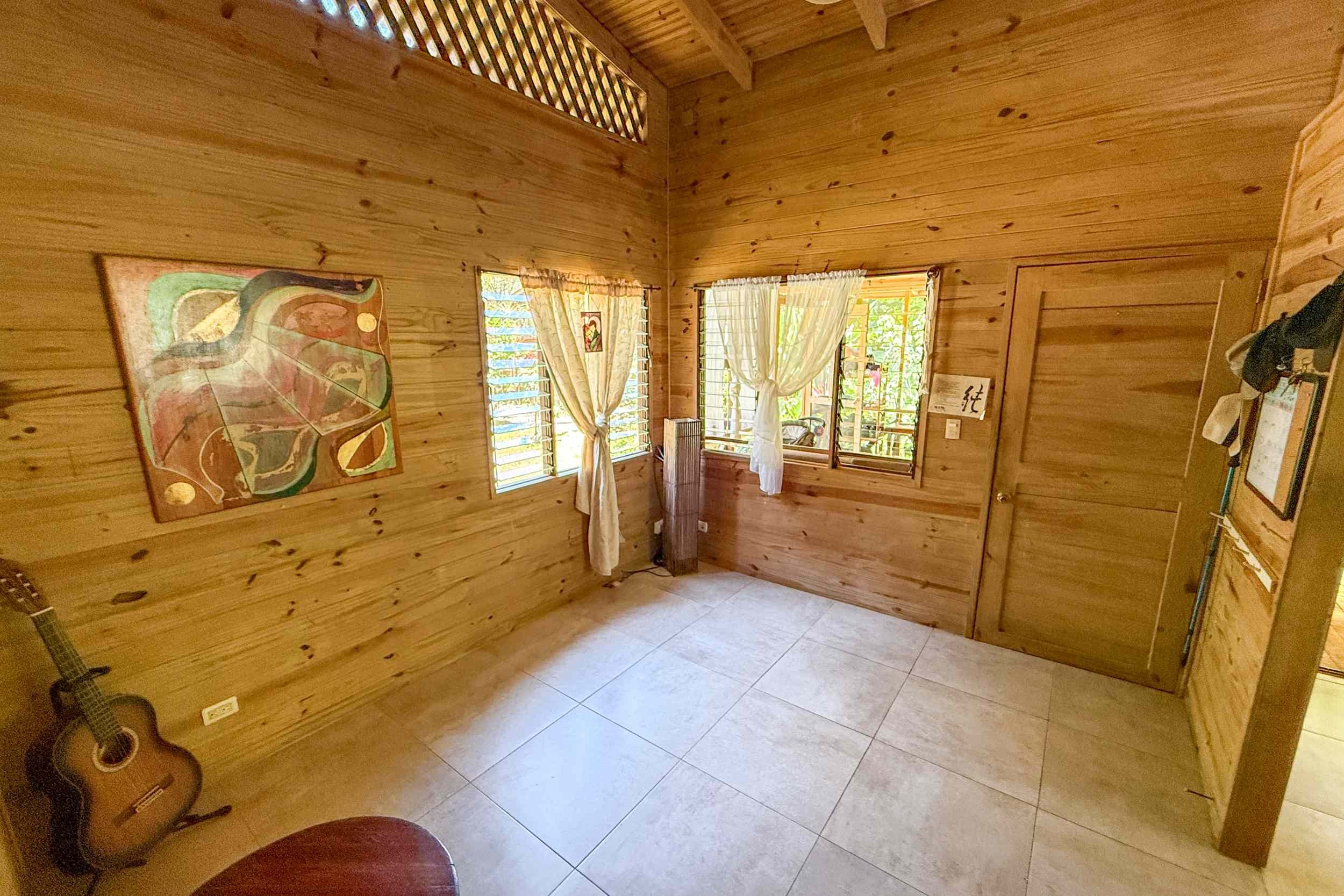 Cozy Wood-Paneled Guest Room Jungle Hotel wood-paneled bedroom with guitar and windows in Ojochal, Costa Rica