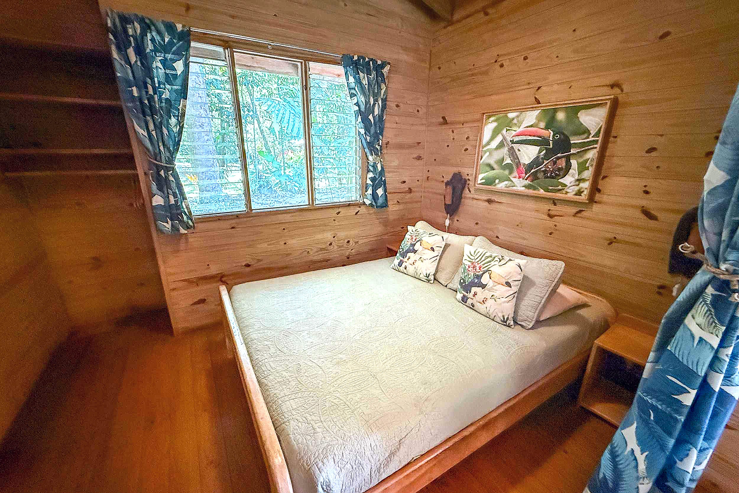 Cozy Wood-Paneled Guest Bedroom Jungle Hotel wooden bedroom with tropical curtains and toucan art in Ojochal, Costa Rica