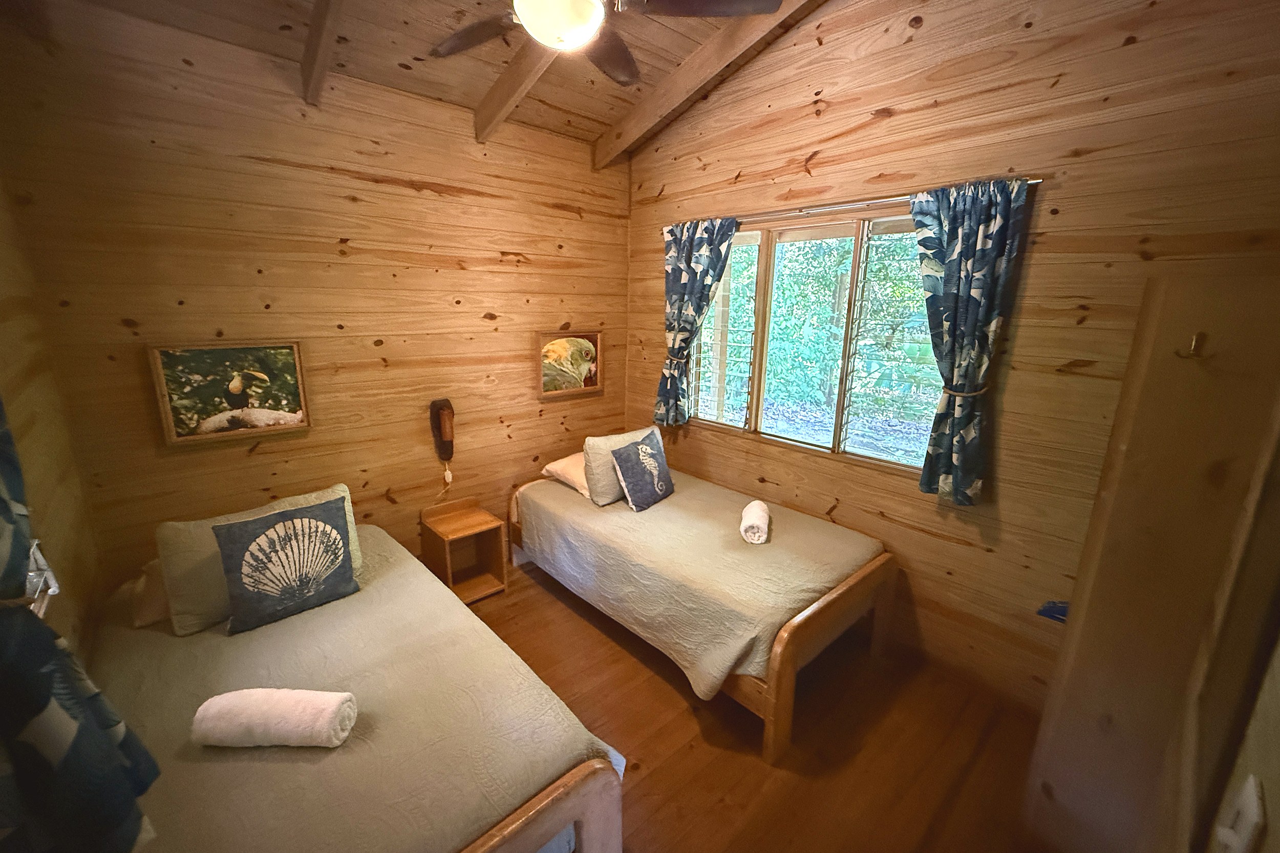 Cozy Wood-Paneled Twin Bedroom Jungle Hotel twin beds with seashell decor in guesthouse bedroom in Ojochal, Costa Rica.
