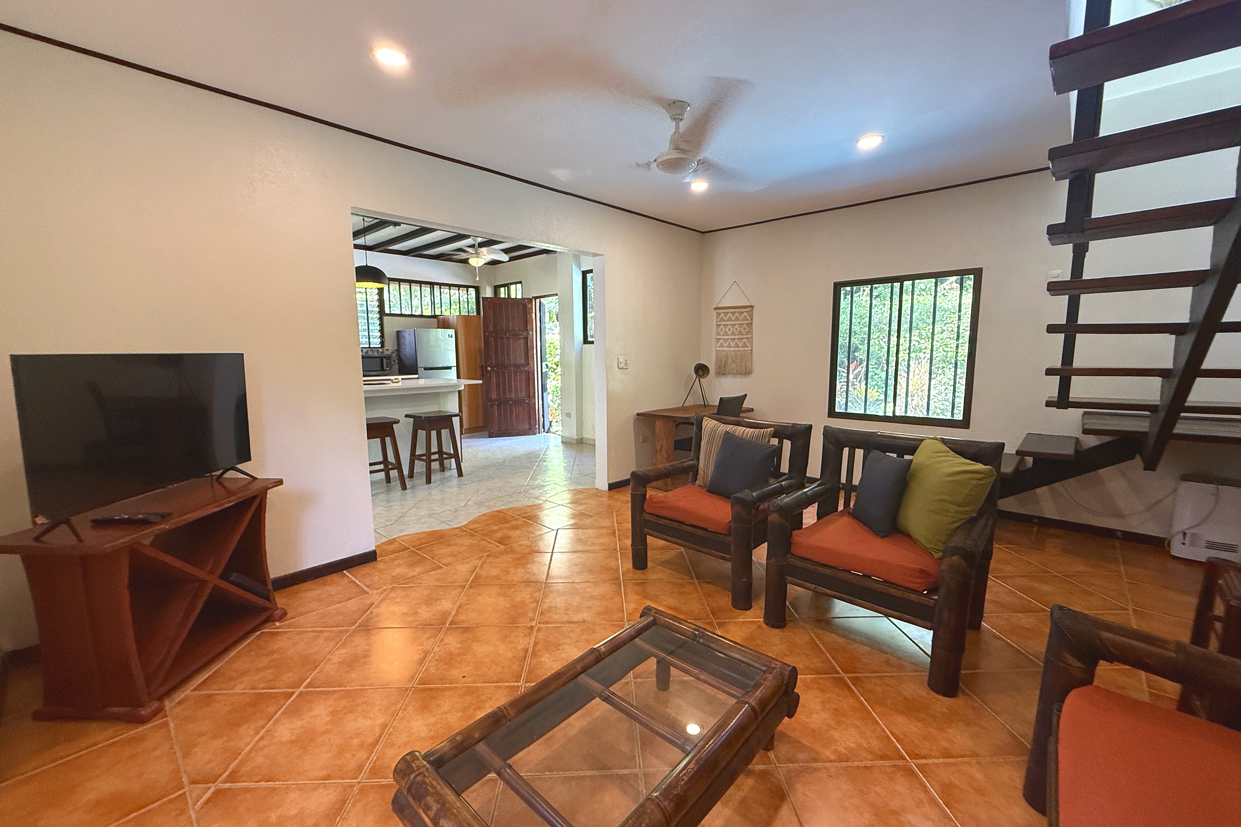Cozy Open-Plan Living Room Jungle Sanctuary living room with wooden armchairs, TV and staircase in Ojochal, Costa Rica