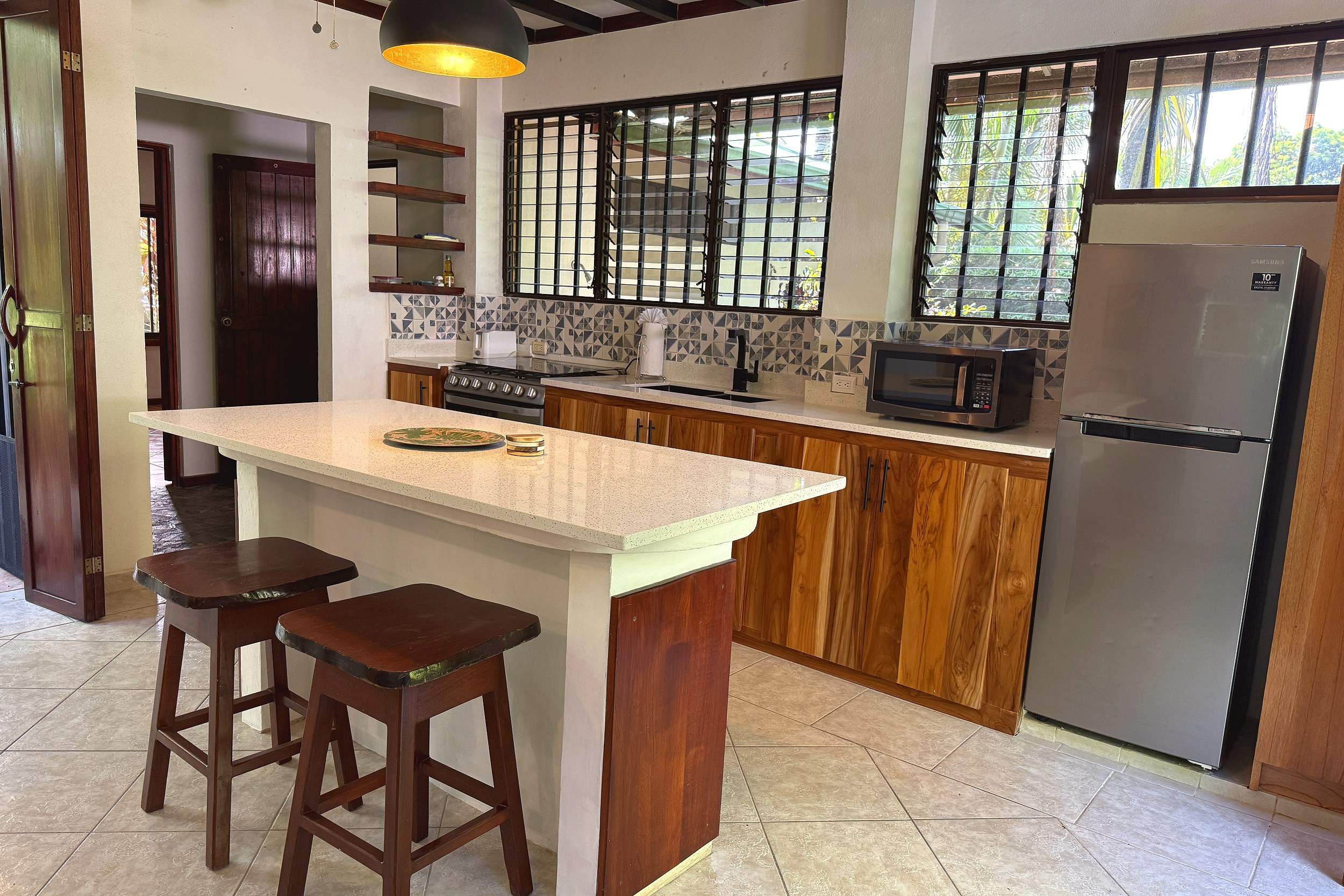 Kitchen Island & Cabinetry Jungle Sanctuary kitchen with wood cabinets, tiled backsplash and island seating in Ojochal, Costa Rica