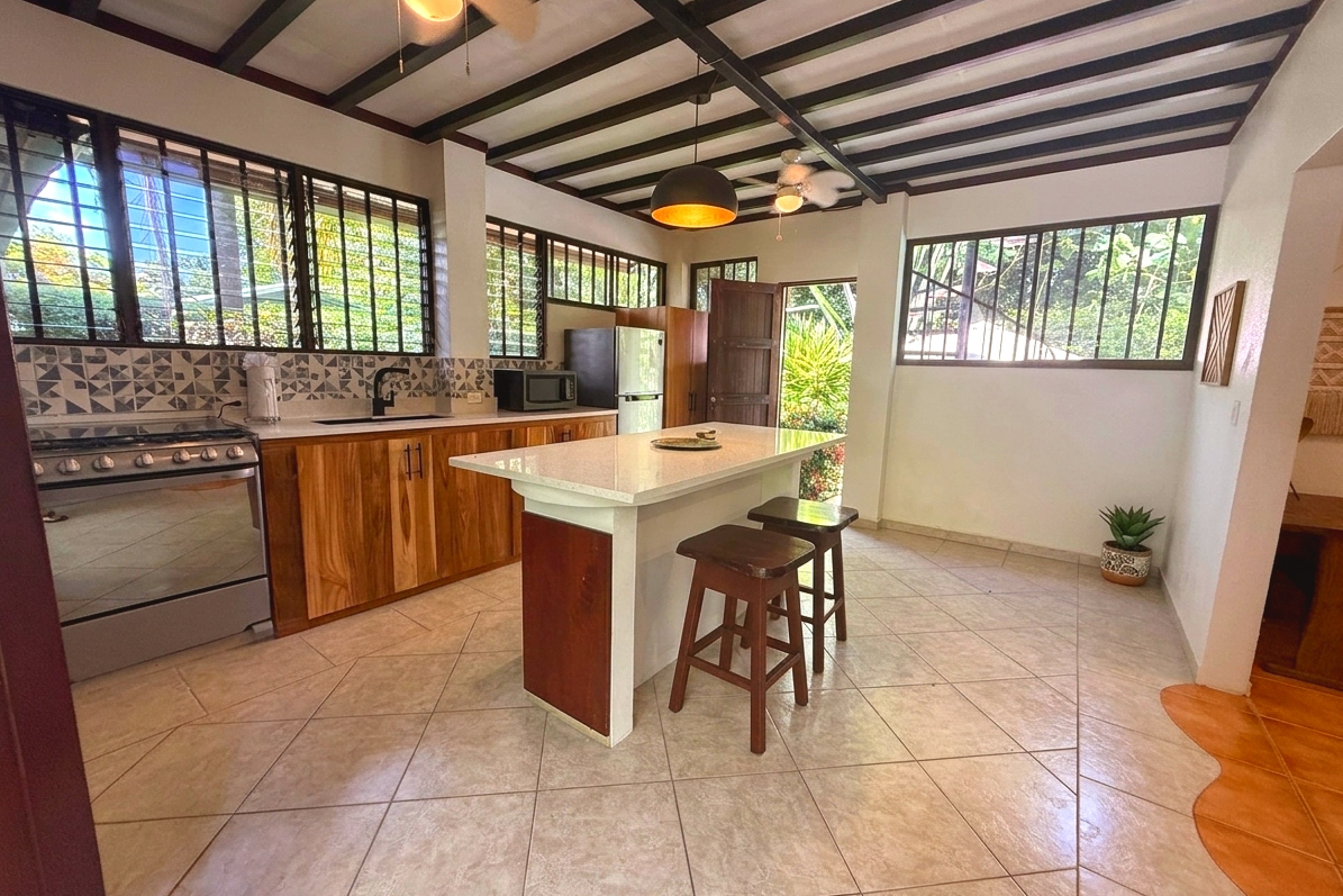 Open Kitchen & Island Jungle Sanctuary kitchen with wood cabinets, island seating, and jungle views in Ojochal, Costa Rica.