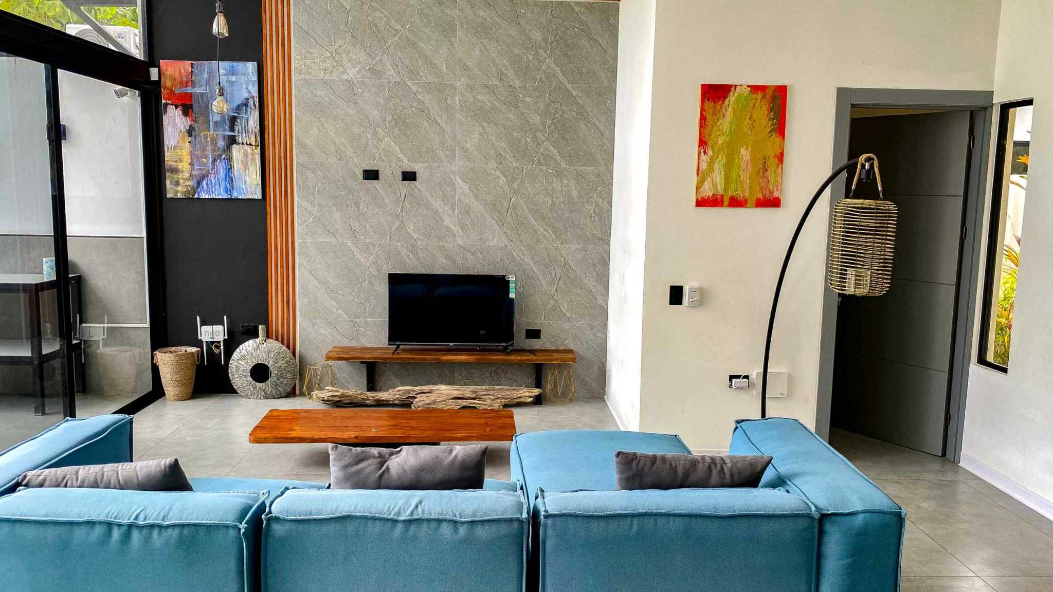 Resort-Style Home living room with teal sofa, marble tile TV wall and abstract art in Uvita, Costa Rica