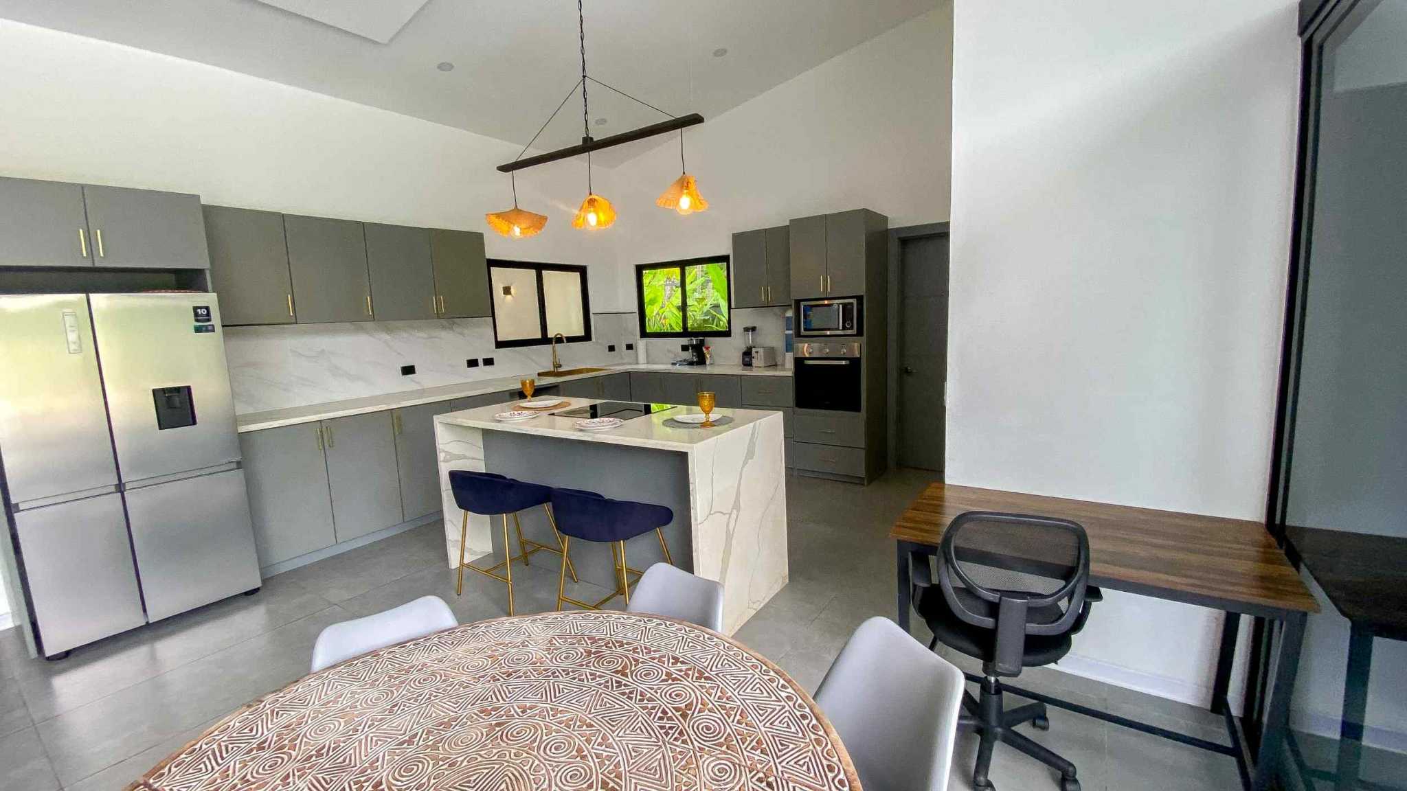 Resort-Style Home kitchen with marble island, gray cabinets and dining table in Uvita, Costa Rica