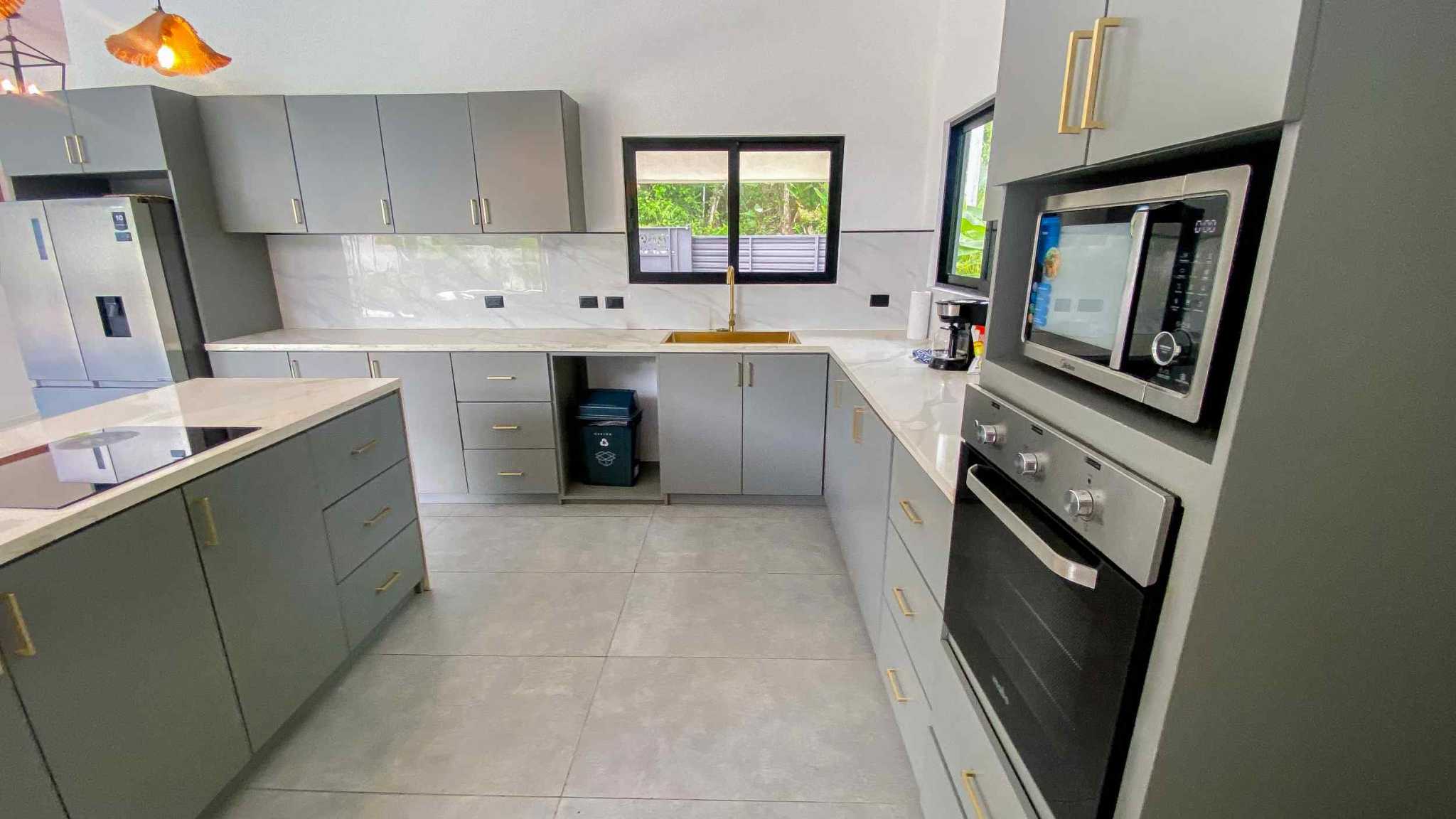 Resort-Style Home modern kitchen with gray cabinets, gold hardware, marble counters and built-in appliances in Uvita, Costa Rica
