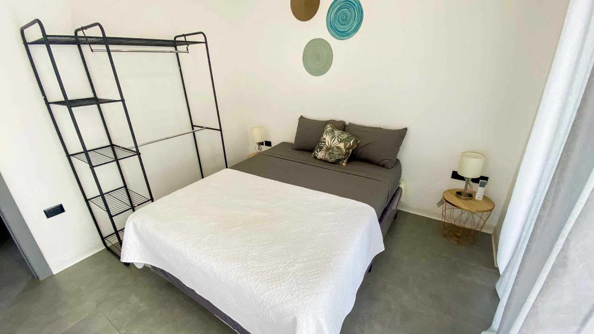 Resort-Style Home bedroom with white quilted bedspread, garment rack, and side table with lamp in Uvita, Costa Rica