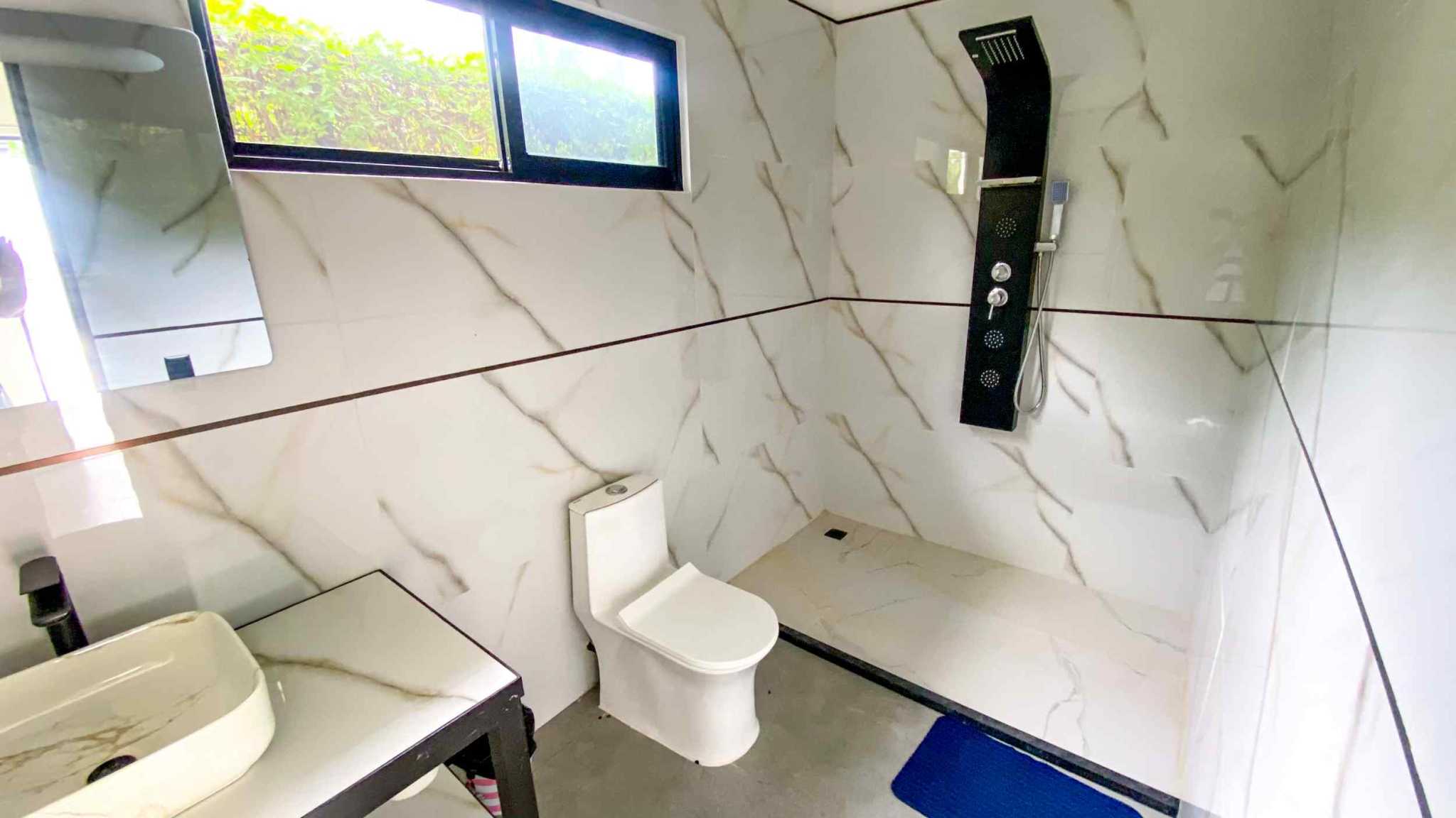 Resort-Style Home bathroom with marble tile, black shower panel, toilet, and vessel sink in Uvita, Costa Rica