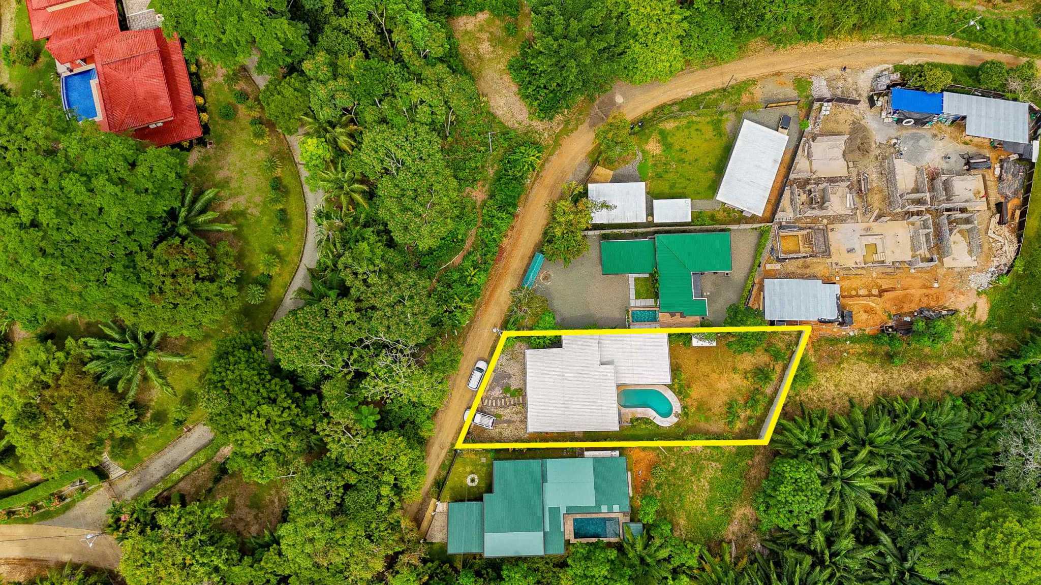 Resort-Style Home aerial view with white roof and curved pool amid tropical trees in Uvita, Costa Rica