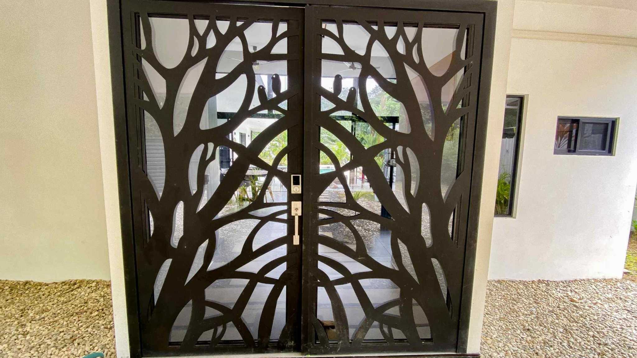 Resort-Style Home decorative tree-branch metal entry doors with glass and pool view beyond in Uvita, Costa Rica