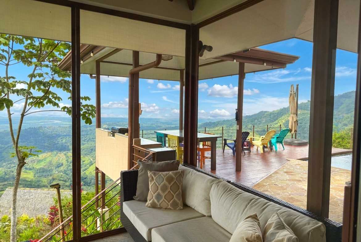 Indoor seating area facing a wooden terrace with panoramic mountain and ocean views in Toucan Valley.